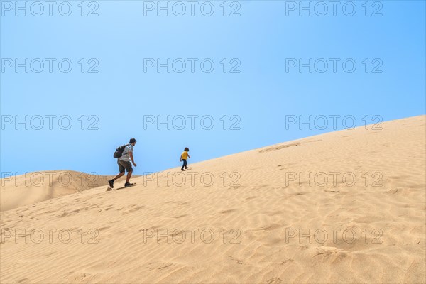 Father and son enjoying climbing the dunes of Maspalomas, Gran Canaria, Canary Islands
