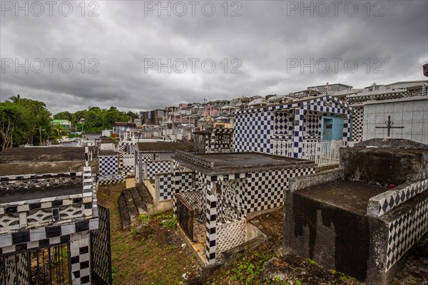 Famous cemetery, many mausoleums or large tombs decorated with tiles, often in black and white. Densely built buildings under a dramatic cloud cover Cimetiere de Morne-a-l'eau, Grand Terre, Guadeloupe, Caribbean, North America