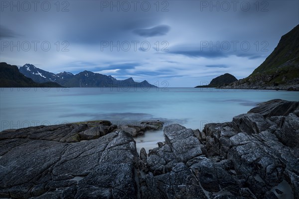 Seascape on the beach at Haukland. View of the mountains of Myrland on Flakstadoya. Dark sky, blurred clouds. Rocks in the foreground. Early summer. Long exposure. Haukland Beach, Haukland, Vestvagoya, Lofoten, Norway, Europe