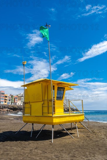 Yellow lifeguard tower in California with green flag in summer by the sea