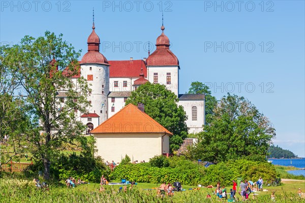 Lacko castle a famous swedish white baroque castle with sunbathing visitors at lake vanern, Laeckoe, Lidkoeping, Sweden, Europe