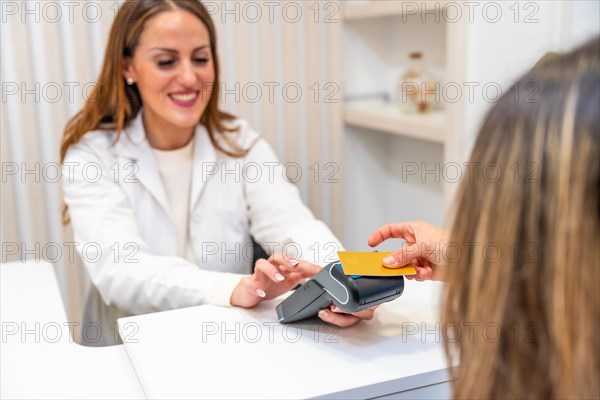 Rear view of a female client paying using credit card in the reception of a beautician clinic