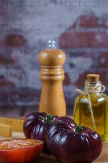 Group of tasty fresh tomatoes of the blue variety together with wooden tongs, a glass bottle of olive oil and a pepper shaker on a wooden table