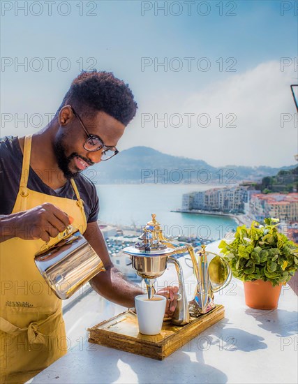 Happy person making coffee outdoors with a scenic coastal view in bright daylight, Vertical aspect ratio, AI generated