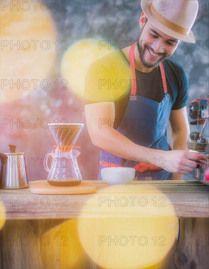 Cheerful man in a blue apron grinds coffee beans, bathed in sunlight with bright yellow orbs, Vertical aspect ratio, AI generated