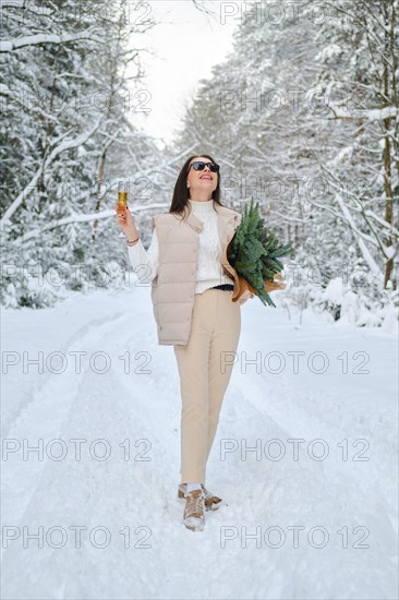 Joyful woman on a forest road with a bouquet of fir branches and a glass of champagne in hand
