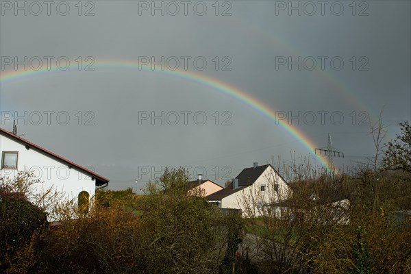 Rainbow over houses and electricity pylons against a blue sky
