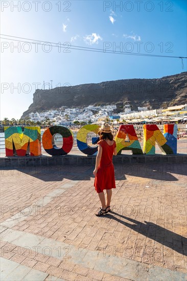 A woman in a red dress on the tourist sign in the coastal town of Mogan in the south of Gran Canaria. Spain