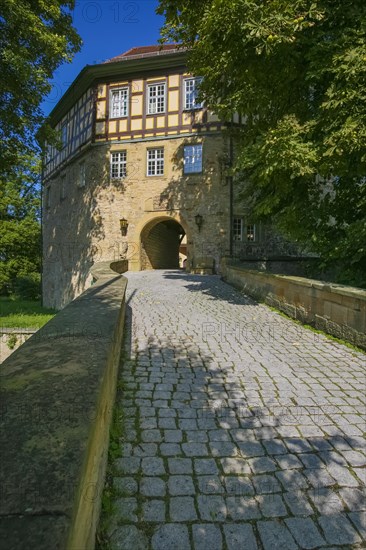 Access to the moated castle Sachsenheim, Grosssachsenheim Castle, former moated castle, archway, cobblestones, path, wall, bridge, crossing, stone figure on the left, relief of the legendary figure Klopferle, castle ghost, coat of arms, with inscription, exterior lights, lamps, architecture, historical building from the 15th century, Sachsenheim, Ludwigsburg district, Baden-Wuerttemberg, Germany, Europe