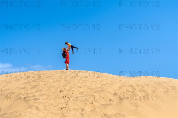 Mother lifting child smiling in the dunes of Maspalomas in summer, Gran Canaria, Canary Islands