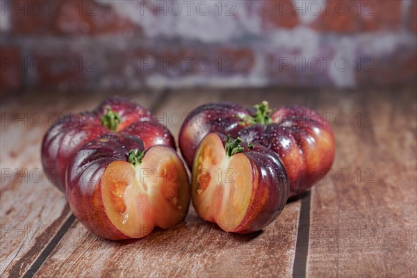 Group of tasty fresh tomatoes of the blue variety with a halved tomato dipped in water drops on a wooden table dipped in water drops on a wooden table
