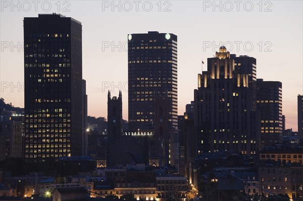 Silhouetted buildings and historic Notre-Dame basilica, art deco Aldred building and modern skyscrapers illuminated at dusk, Old Montreal, Quebec, Canada, North America