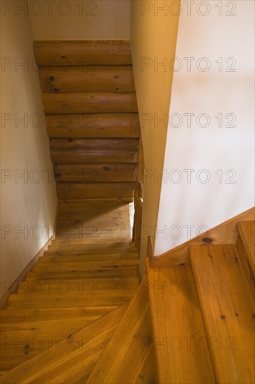 Narrow steep and twisting pine wood staircase with natural stained steps and rustic log wall leading to downstairs floor inside Scandinavian style log cabin home, Quebec, Canada, North America