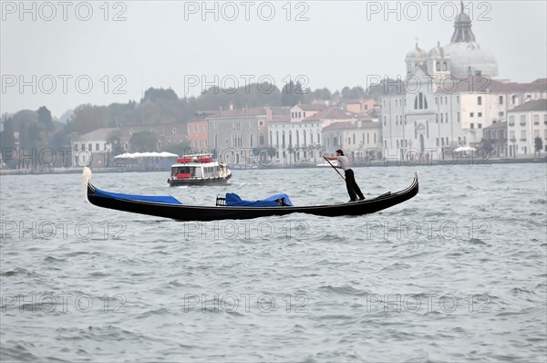 Gondolier paddling a gondola against the backdrop of historic buildings, Venice, Veneto, Italy, Europe