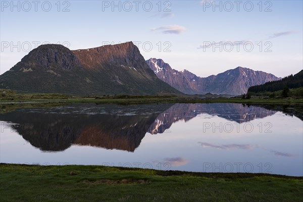 Landscape on the Lofoten Islands. Vagspollen bay, with Offersoykammen mountain behind it. The mountain Stornappstinden on Flakstadoya in the background. The mountains are reflected in the water. At night at the time of the midnight sun in good weather. Early summer. Vestvagoya, Lofoten, Norway, Europe