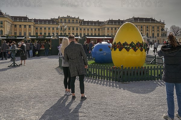 A couple looks at a large, decorative Easter egg in front of the magnificent Schoenbrunn Palace Easter Market