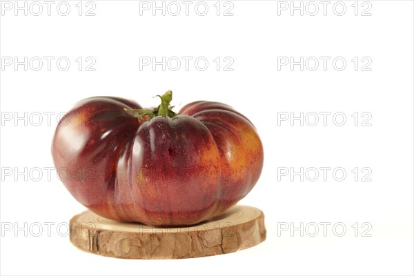 Close-up of a delicious fresh tomato of blue variety isolated on a white background on a wooden disk