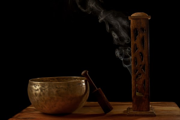 Tibetan singing bowl next to a wooden censer with smoke coming out isolated on black background with copy space