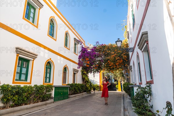 A tourist woman with a red dress in the port of Mogan town full of flowers in Gran Canaria in summer. Spain