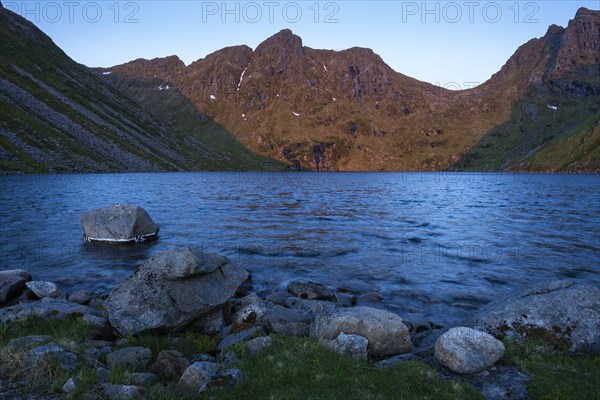 Lake Utdalsvatnet at night at the time of the midnight sun in good weather, blue sky. The mountain Hogskolmen is illuminated by the night sun. Unstad, Vestvagoya, Lofoten, Norway, Europe