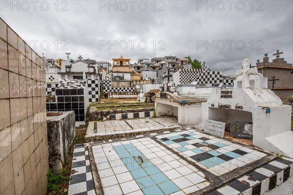 Famous cemetery, many mausoleums or large tombs decorated with tiles, often in black and white. Densely built buildings under a dramatic cloud cover Cimetiere de Morne-a-l'eau, Grand Terre, Guadeloupe, Caribbean, North America