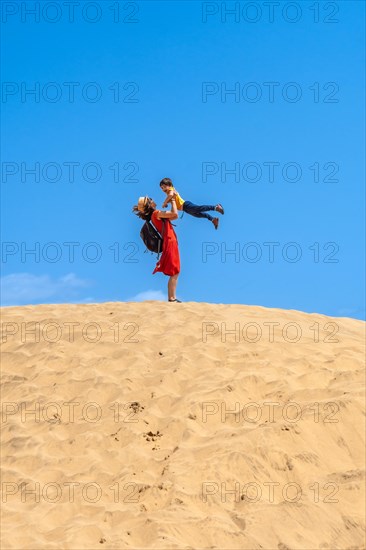 Mother lifting child smiling in the dunes of Maspalomas on vacation, Gran Canaria, Canary Islands
