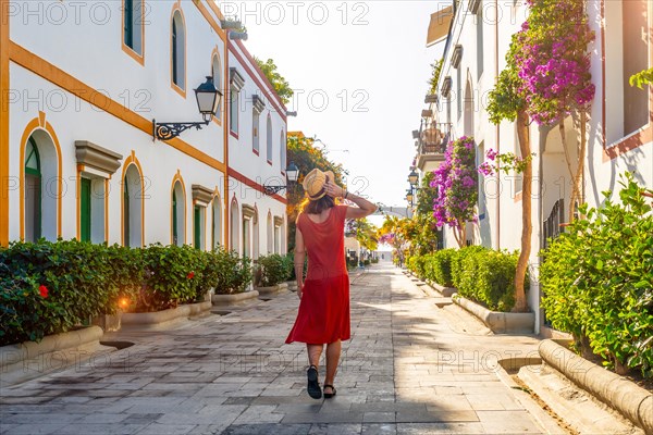 A woman walking in a red dress in the port of the flower-filled coastal town Mogan in the south of Gran Canaria. Spain