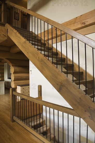 Brown stained wooden staircase with wrought iron railing leading to upstairs floor from living room inside luxurious contemporary Scandinavian style log cabin home, Quebec, Canada, North America