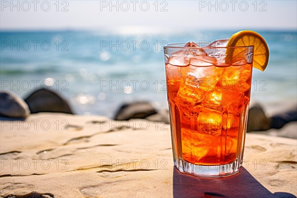 Glass with orange cocktail drink with ice cubes and orange fruit slice with beach in background. KI generiert, generiert, AI generated