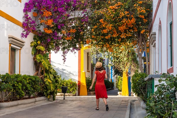A tourist woman with a red dress in the port of Mogan town full of flowers in Gran Canaria in summer