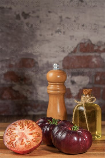 Group of tasty fresh tomatoes of the blue variety together with wooden tongs, a glass bottle of olive oil and a pepper shaker on a wooden table
