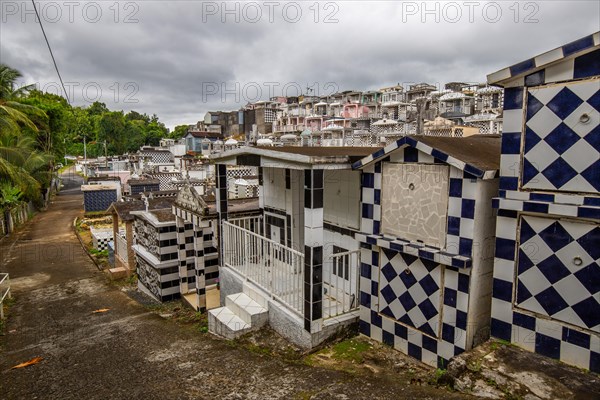 Famous cemetery, many mausoleums or large tombs decorated with tiles, often in black and white. Densely built buildings under a dramatic cloud cover Cimetiere de Morne-a-l'eau, Grand Terre, Guadeloupe, Caribbean, North America