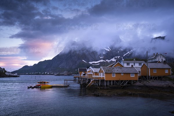 The village of Sakrisoy with its typical yellow or ochre-coloured wooden houses on wooden stilts (rorbuer) by the sea. At night at the time of the midnight sun. Some colourful clouds in the sky. Early summer. Sakrisoy, Moskenesoya, Lofoten, Norway, Europe