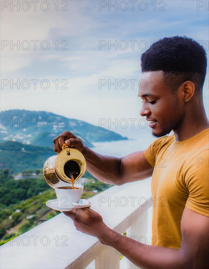 African young stylish Man pouring coffee from a golden coffee maker on a terrace with a serene mountain view, Vertical aspect ratio, AI generated