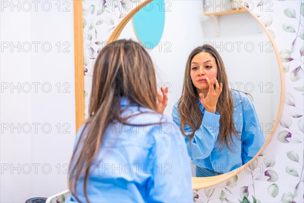 Adult caucasian woman looking herself in a mirror after rejuvenation facial treatment in the clinic