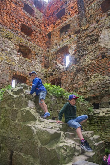 Two boys climbing in the tower in Hammershus which was Scandinavia's largest medieval fortification and is one of the largest medieval fortifications in Northern Europe. Now ruin and located on the island Bornholm, Denmark, Baltic Sea, Scandinavia, Europe