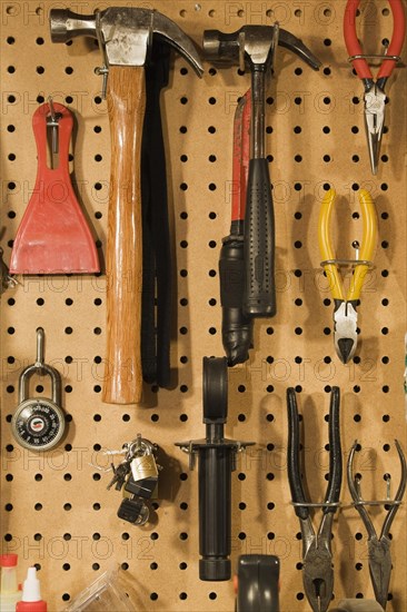 Assorted hand tools that include a small and medium hammer, red needle nose pliers, yellow wire cutter, standard black pliers on pegboard wall in workshop, Studio Composition, Quebec, Canada, North America