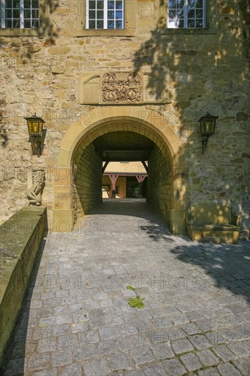 Access to the moated castle Sachsenheim, Grosssachsenheim Castle, former moated castle, archway, cobblestones, path, wall, stone figure on the left, relief of the legendary figure Klopferle, castle ghost, coat of arms, with inscription, exterior lights, lamps, architecture, historical building from the 15th century, Sachsenheim, Ludwigsburg district, Baden-Wuerttemberg, Germany, Europe