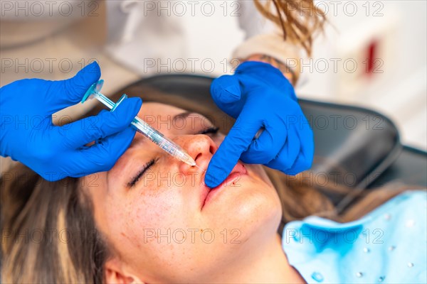 Close-up of the hands of a female doctor applying botox therapy on lips of an adult caucasian woman
