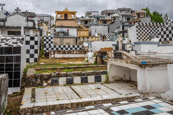 Famous cemetery, many mausoleums or large tombs decorated with tiles, often in black and white. Densely built buildings under a dramatic cloud cover Cimetiere de Morne-a-l'eau, Grand Terre, Guadeloupe, Caribbean, North America