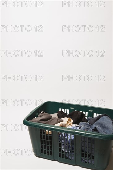 Close-up of green plastic laundry hamper or basket filled with various dirty clothes that includes blue jeans, t-shirts on white background, Studio Composition, Quebec, Canada, North America