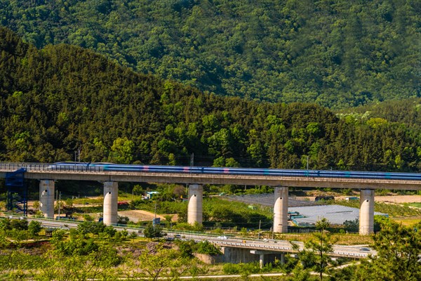 High-speed train on a bridge with green rolling hills under the bright sunlight, in South Korea