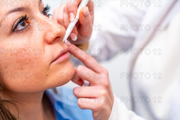 Close-up of the hands of a cosmetologist marking the points to inject hyaluronic acid on the patient's face using marker in the clinic
