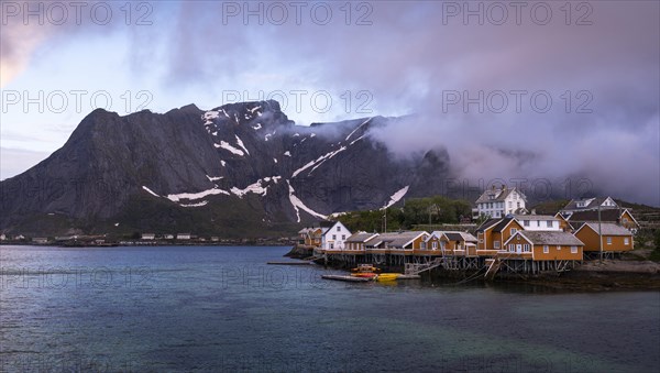 The village of Sakrisoy with its typical yellow or ochre-coloured wooden houses on wooden stilts (rorbuer) by the sea. At night at the time of the midnight sun. A few clouds in the sky. Early summer. Sakrisoy, Moskenesoya, Lofoten, Norway, Europe