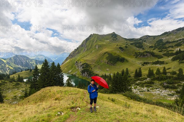 Woman 60-65 hiking with umbrella, behind her Seealpsee and Seekoepfel, 1919m, Allgaeu Alps, Allgaeu, Bavaria, Germany, Europe