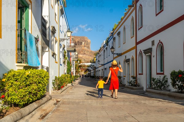 Mother in a red dress and her son walking in the port of the town Mogan in Gran Canaria. Family vacation