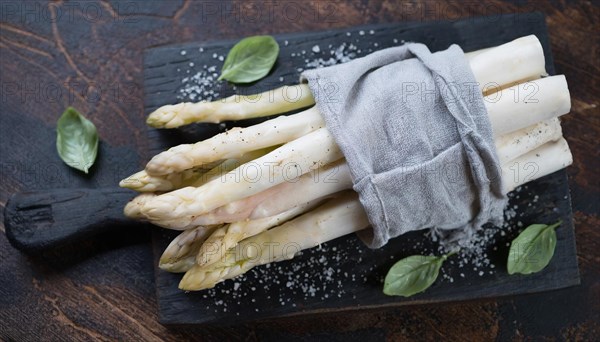 White asparagus on a chopping board with basil and a pinch of salt, bunch of white asparagus wrapped in damp kitchen towel, KI generated, AI generated