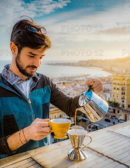 A focused man pours hot water for coffee on a balcony, with a serene sea view in the warm morning light, Vertical aspect ratio, AI generated