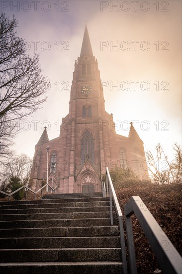 Sunbeams illuminate a church accessible via a staircase with metal railing, sunrise, Nagold, Black Forest, Germany, Europe