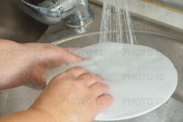 Woman washing dishes in kitchen sink, closeup view. Cleaning chores